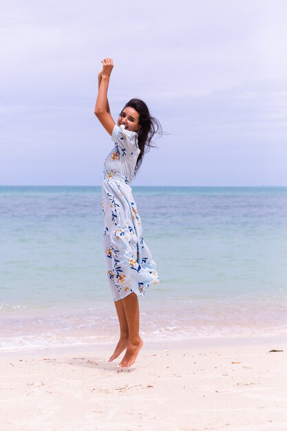 Romantic portrait of woman in long blue dress on beach by sea at windy day