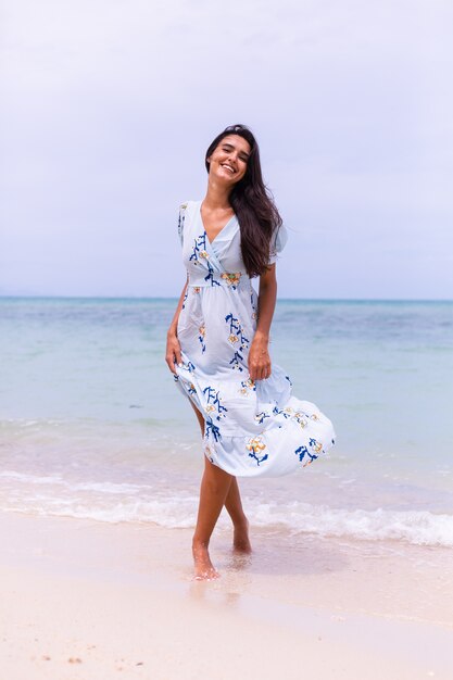 Romantic portrait of woman in long blue dress on beach by sea at windy day