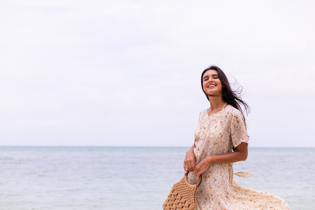 Romantic portrait of woman in long dress on beach at windy cloudy day.