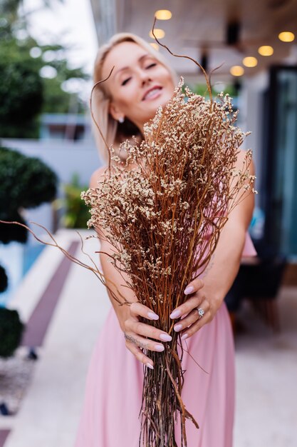 Romantic portrait of woman in pink evening cute dress hold wild flowers outside luxury tropical villa Beautiful female with bouquet