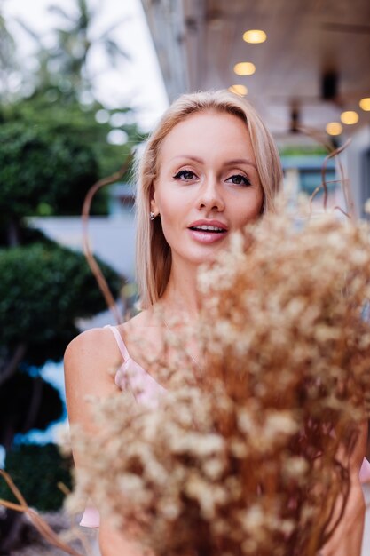 Romantic portrait of woman in pink evening cute dress hold wild flowers outside luxury tropical villa Beautiful female with bouquet