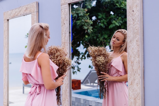 Romantic portrait of woman in pink evening cute dress hold wild flowers outside luxury tropical villa Beautiful female with bouquet