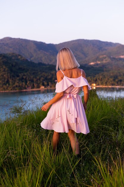 Romantic portrait of young caucasian woman in summer dress enjoying relaxing in park on mountain with amazing tropical sea view Female on vacation travel around Thailand Happy woman at sunset