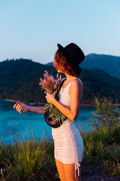 Romantic portrait of young caucasian woman in summer dress enjoying relaxing in park on mountain with amazing tropical sea view