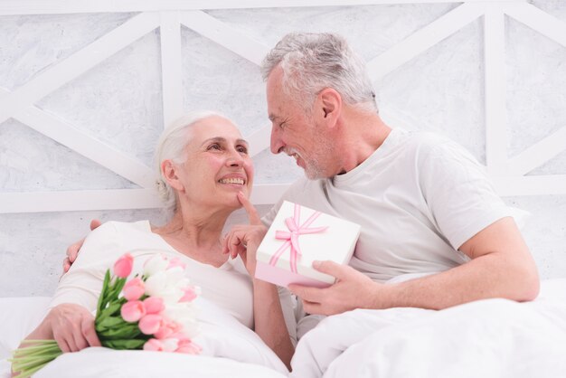 Romantic senior couple looking at each other holding bouquet and gift box in had