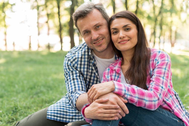 Foto gratuita coppie sorridenti romantiche che si siedono nel parco che guarda l'obbiettivo