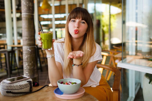 ロマンチックな笑顔の女性はキスを送信し、健康的なビーガンの朝食を食べます。