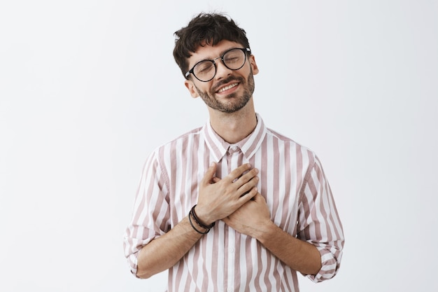 Romantic stylish bearded guy posing against the white wall with glasses