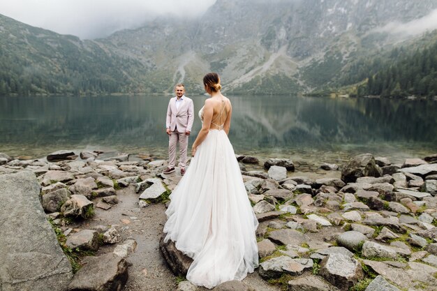 ポーランドのシーアイ湖の愛立っているロマンチックな結婚式のカップル。タトラ山脈。