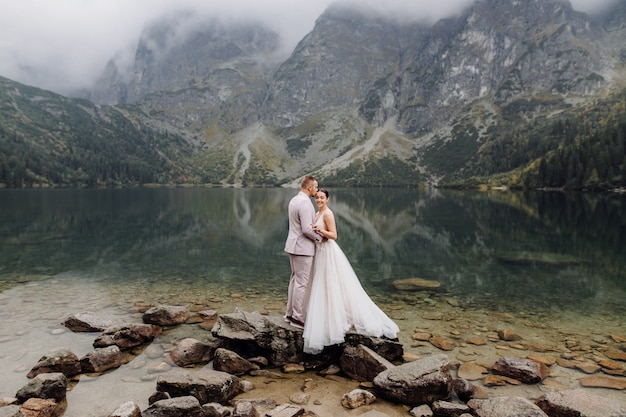 ポーランドのシーアイ湖の愛立っているロマンチックな結婚式のカップル。タトラ山脈。