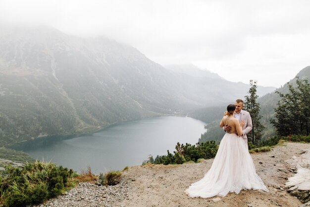 ポーランドのシーアイ湖の愛立っているロマンチックな結婚式のカップル。タトラ山脈。