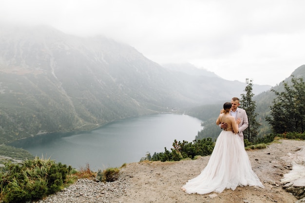 ポーランドのシーアイ湖の愛立っているロマンチックな結婚式のカップル。タトラ山脈。