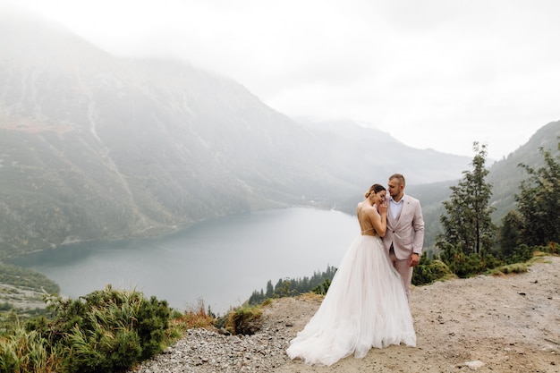 ポーランドのシーアイ湖の愛立っているロマンチックな結婚式のカップル。タトラ山脈。