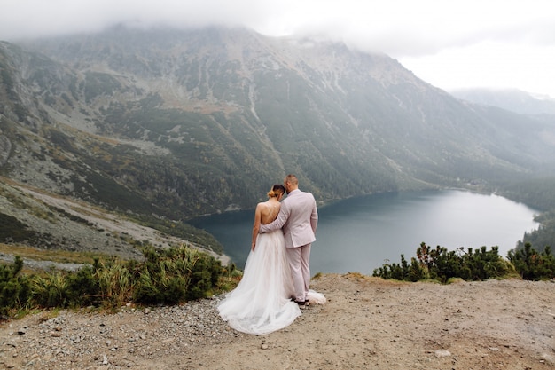 ポーランドのシーアイ湖の愛立っているロマンチックな結婚式のカップル。タトラ山脈。