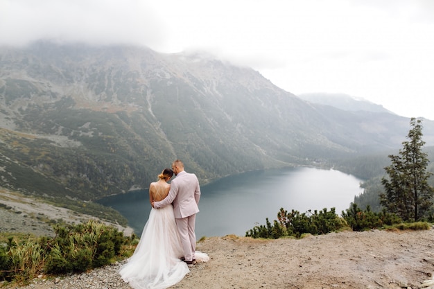 ポーランドのシーアイ湖の愛立っているロマンチックな結婚式のカップル。タトラ山脈。