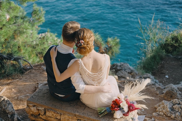 Foto gratuita la coppia di sposi romantiche si siede sullo sfondo di una bellissima isola nel mare e gode di una splendida vista sul montenegro