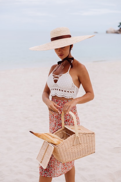 Романтичная женщина на пляже в вязаном топе с юбкой и соломенной шляпе держит корзину с хлебом Eco life