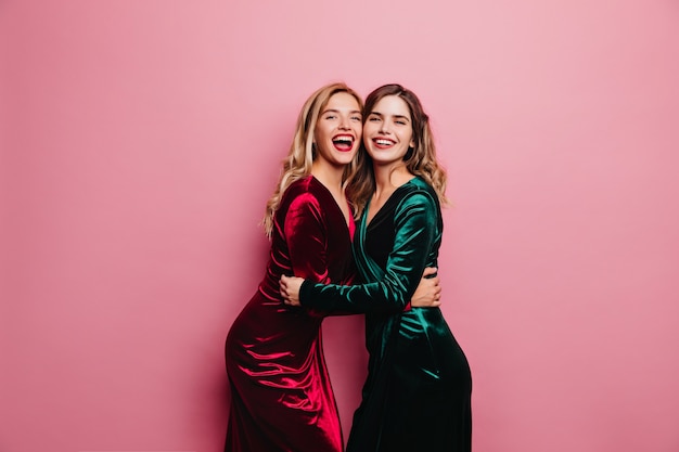 Romantic woman in green dress embracing her sister. Happy caucasian girls in velvet outfit laughing