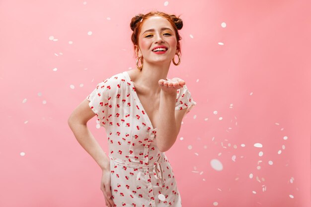 Romantic woman in light dress posing on pink background with white confetti