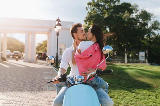 Романтичная женщина в розовой одежде нежно трогает своего парня с любовью, сидя на скутере