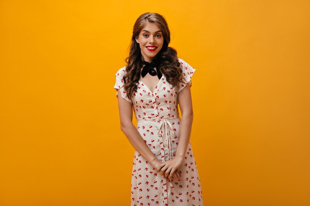 Romantic woman in white dress poses on orange background.Lovely girl with wavy hair in modern outfit looking into camera.