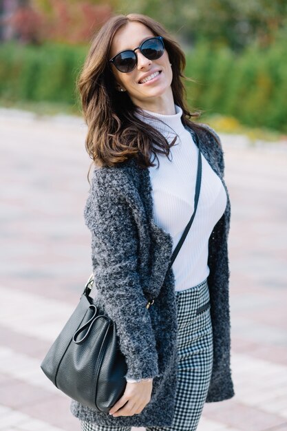 Romantic woman with dark hairstyle in gray jacket enjoying walking outside