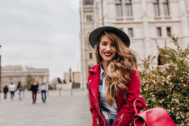 Romantic woman with long curly hairstyle posing with smile during travel around Europe