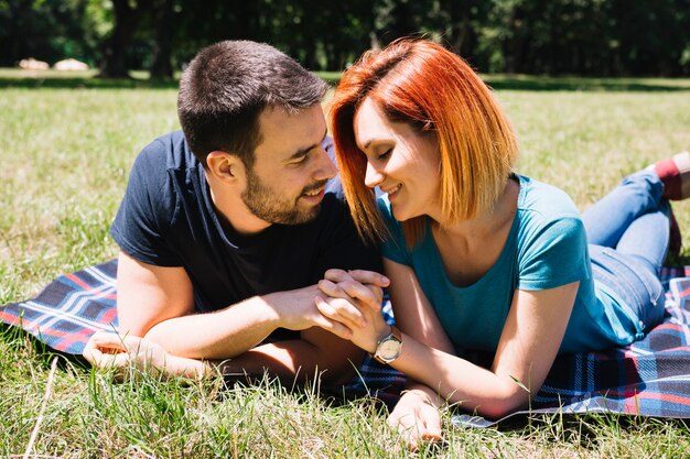 Romantic young couple holding each other hands lying on blanket in the park