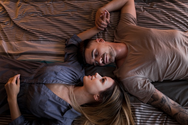 Free photo romantic young couple lying on bed holding each other's hand