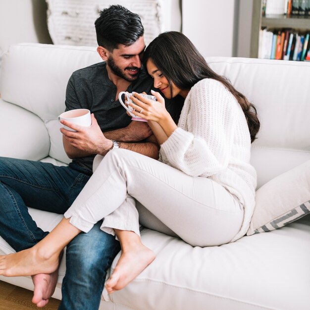 Romantic young couple sitting on white sofa holding coffee cup