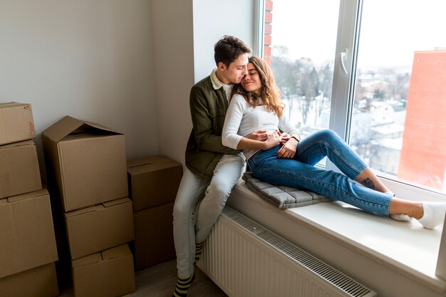 romantic young couple sitting on window sill in their new apartment
