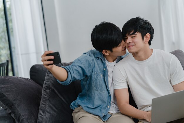 집에서 핸드폰으로 로맨틱 젊은 게이 커플 재미 selfie. 아시아 연인 남성 행복 기술 휴대 전화 웃 고 거실에서 소파에 누워있는 동안 사진을 함께 사용 하여 재미를 휴식.