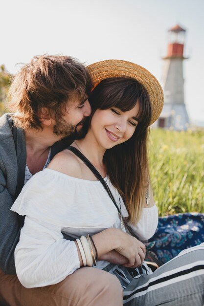 Romantic young hipster couple indie style in love walking in countryside, lighthouse on background, summer vacation