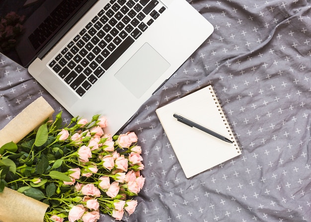 Rose bouquet; pen; spiral notepad and laptop on gray textile