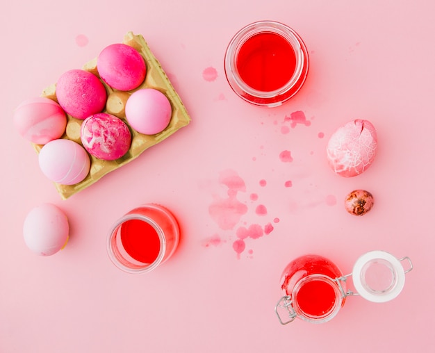 Розовые пасхальные яйца возле банки с жидкостью для красителя