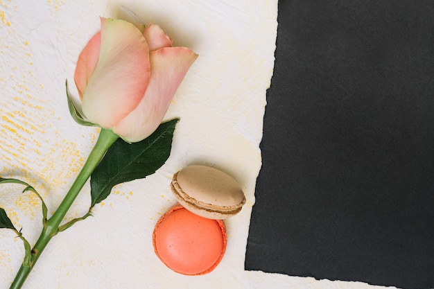 Fiore di rosa con biscotti e carta nera sul tavolo