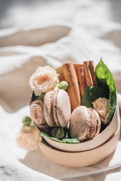 Rose flowers with macaroons and cinnamon on container over the white cloth