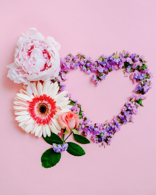 Роза, гербера и цветок пиона с сердечком на розовом фоне