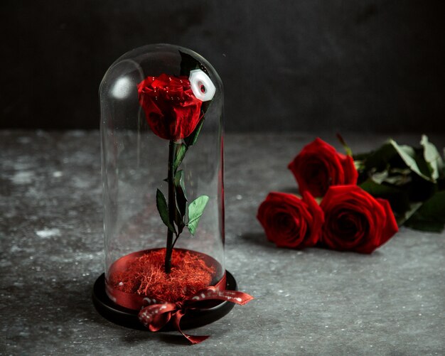роза в стеклянном куполе и красные розы на столе