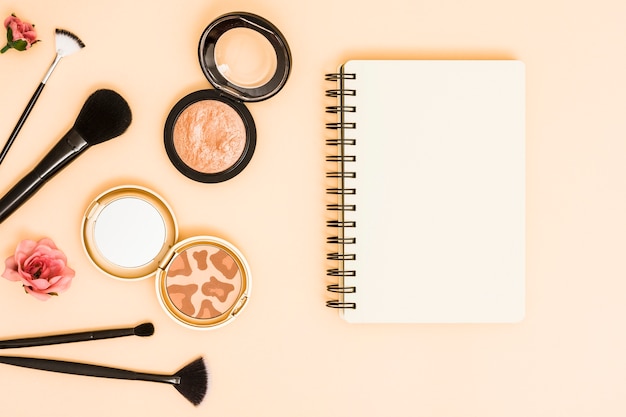 Rose; makeup brushes and compact powder near the spiral notepad on beige backdrop