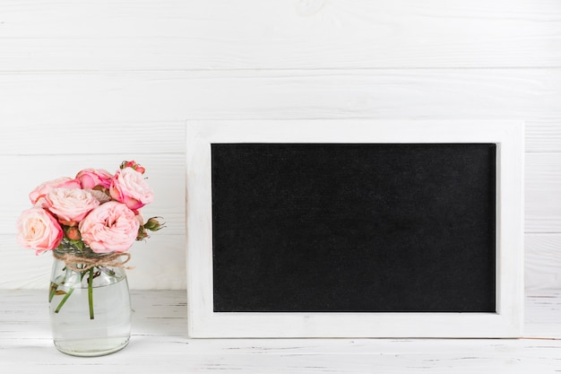 Rose vase near the blank frame on desk against white plank textured background