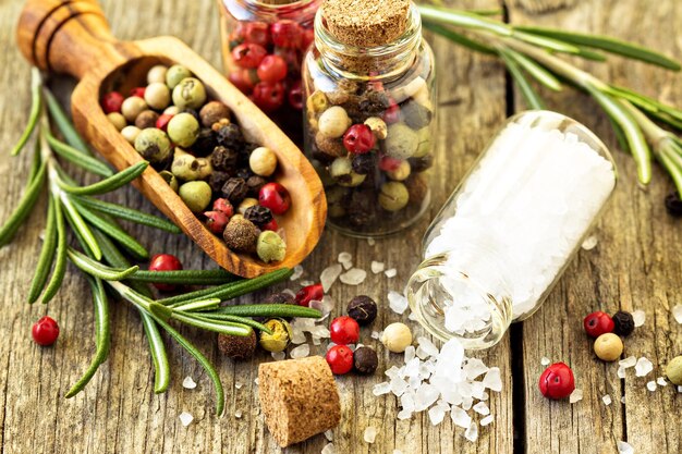 Rosemary salt and different kinds of pepper on wooden table