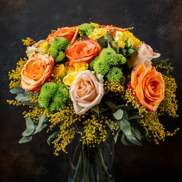 Букет из роз с оранжевыми, желтыми розами, мимозой на темном фоне