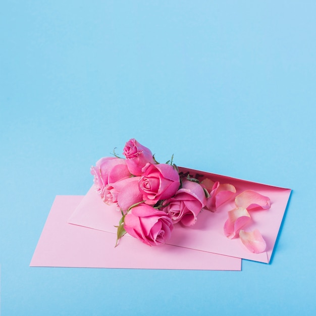 Roses buds with envelope on blue table