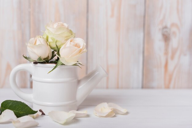 Roses in the ceramic small watering can on wooden desk