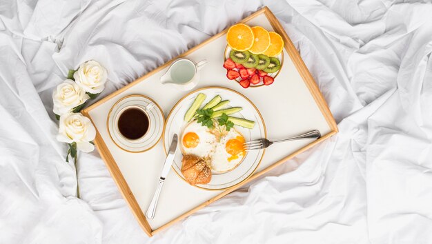 Roses and healthy breakfast tray on crumbled bed