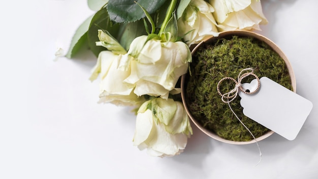 Roses and wedding rings with white tag on moss in the bowl