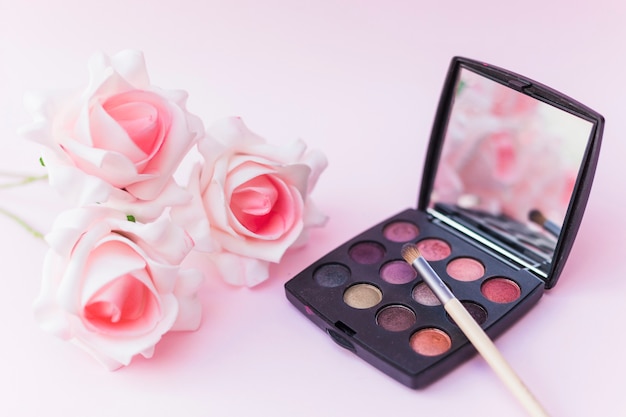 Roses with makeup brush and eyeshadow palette on pink backdrop