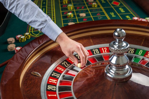 Roulette wheel and croupier hand with white ball in casino close up details