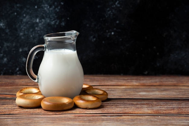 Round biscuits and glass jug of milk on wooden table. 